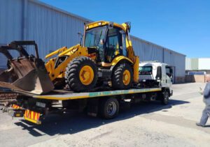folami towing flatbed truck moving a yellow tractor